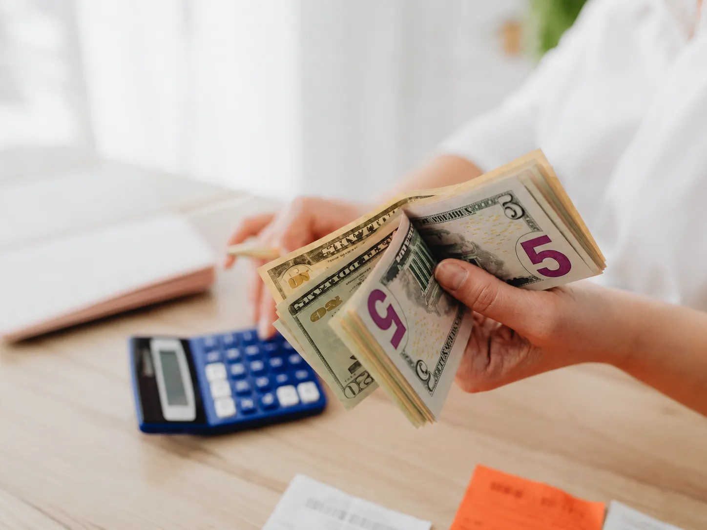 Person counting US dollar bills beside a calculator
